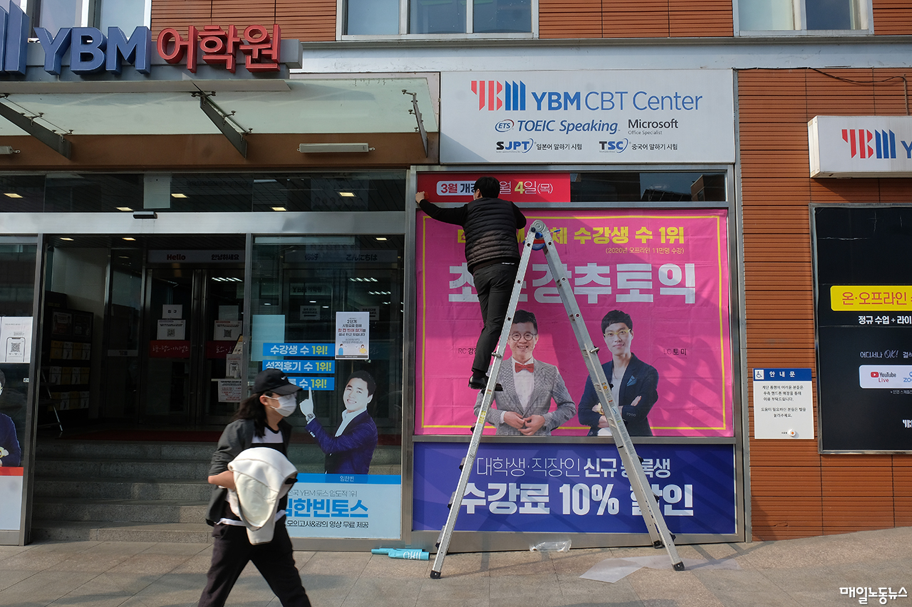 서울 신촌의 한 어학원 입구에서 직원이 사다리에 올라 새학기 수업 광고를 붙이고 있다.  <정기훈 기자>