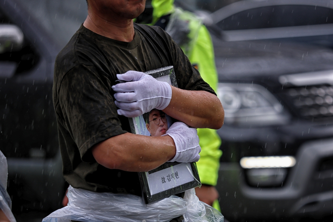 아리셀 참사 유가족들이 비를 가리려 영정을 품에 안고 있다. <윤성희 기자>